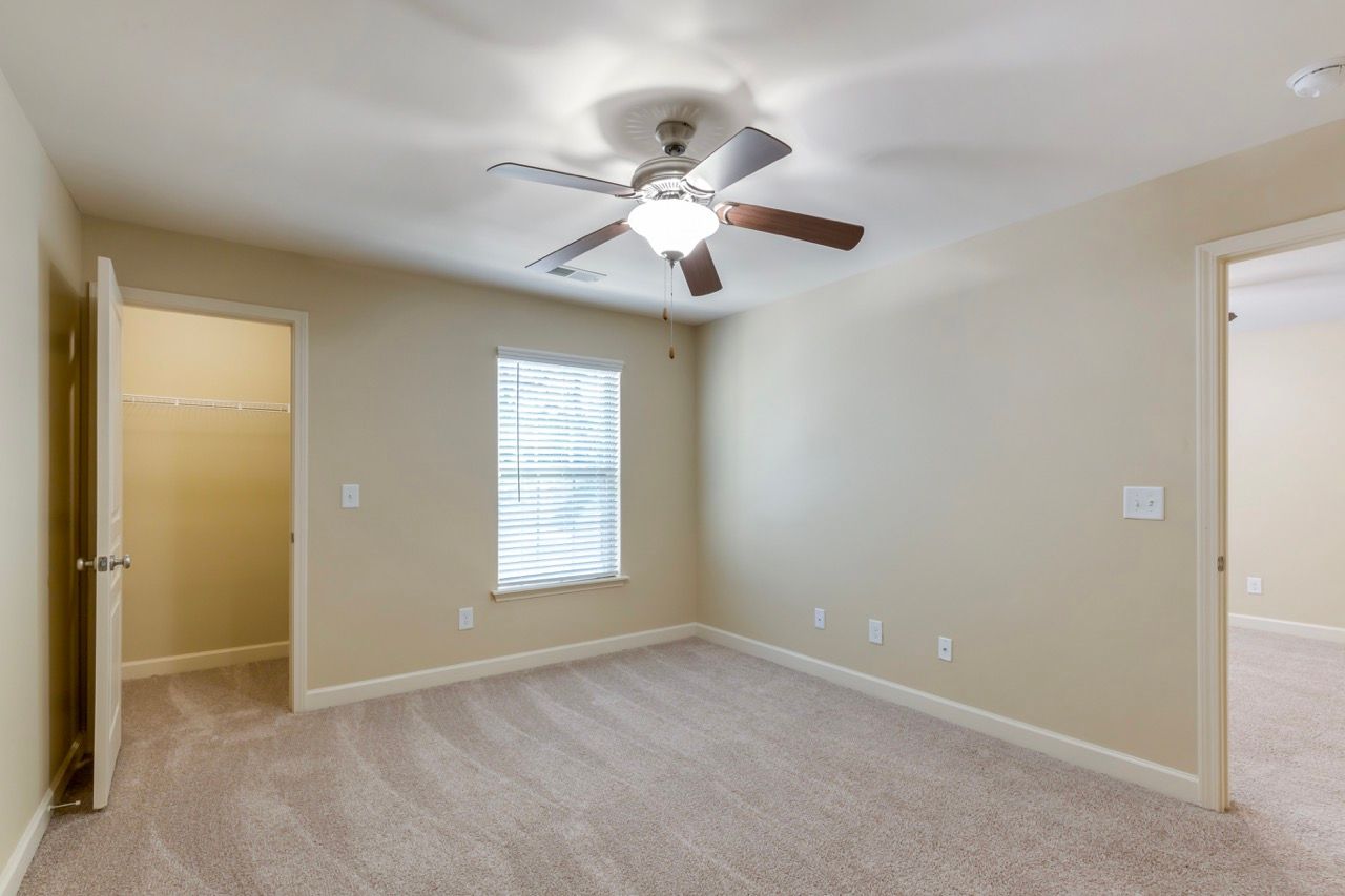Bedroom with beige walls, white trim, ceiling fan, window with blinds, and carpet.