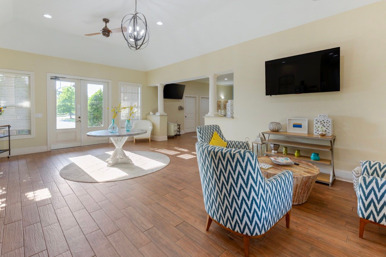 Furnished living area in a model apartment with blue chevron chairs, round table, and wall-mounted TV.