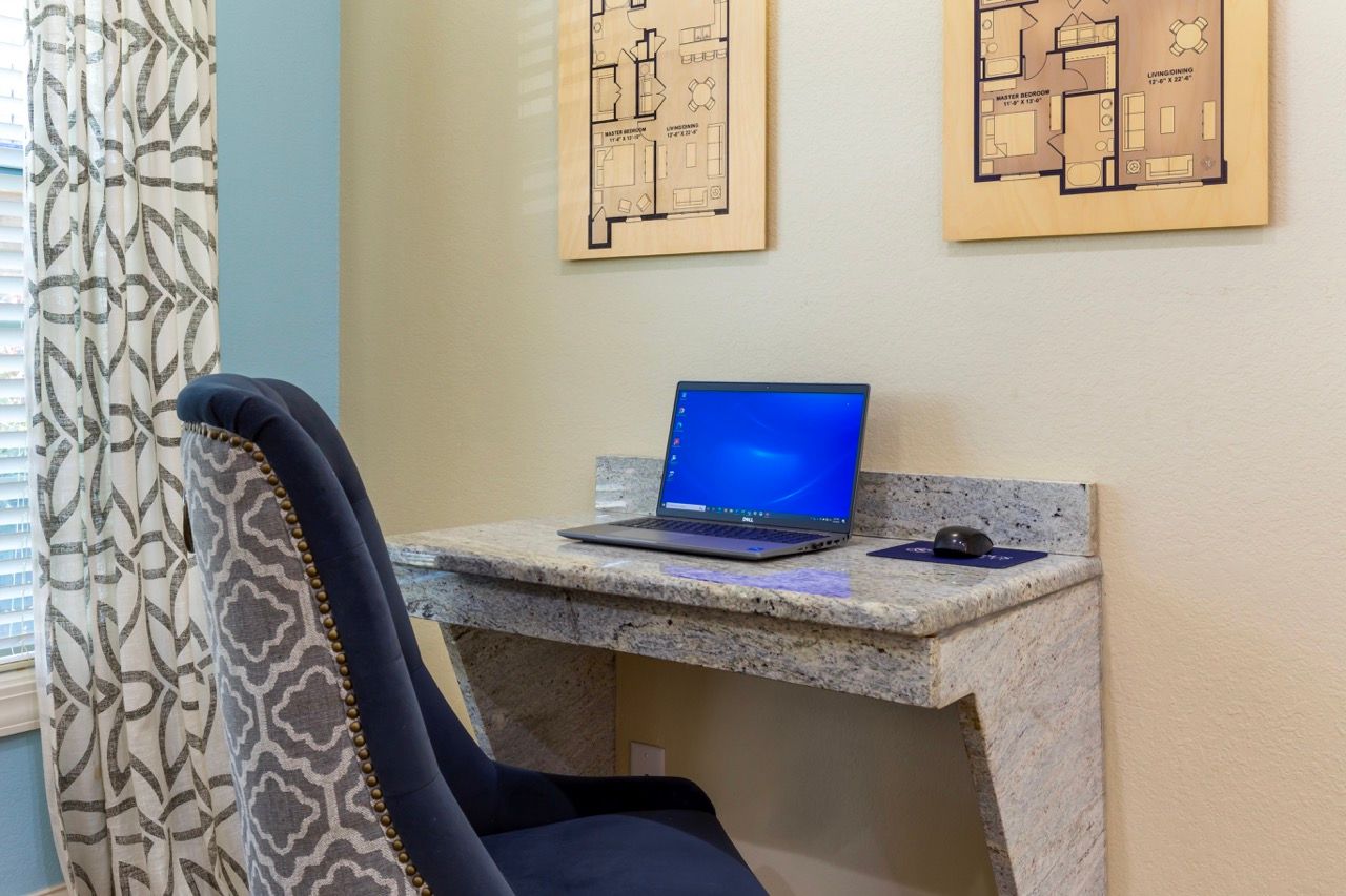Home office nook with marble desk, laptop, and patterned upholstered chair.