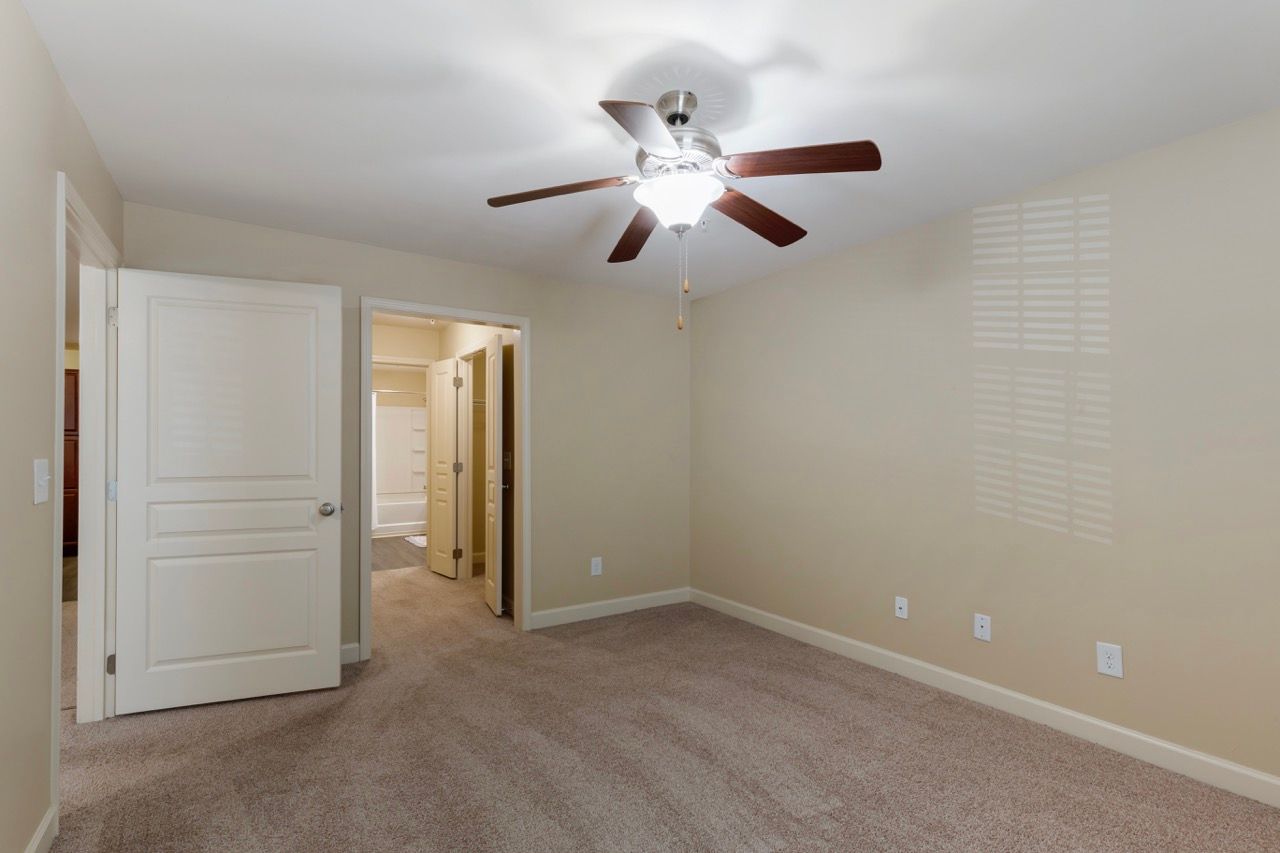 Bedroom interior with beige walls, ceiling fan, and carpet.