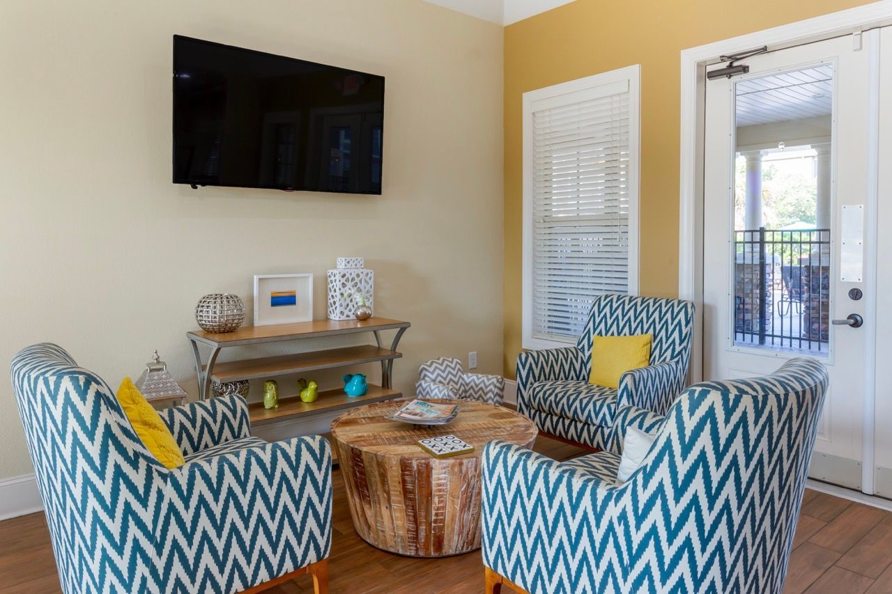 Apartment living room with blue chevron chairs, a round wood coffee table, and a wall-mounted TV.