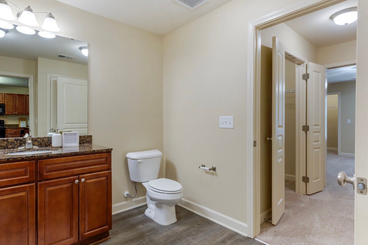Bathroom with wood vanity, granite countertop, toilet, and doorway to the hallway.
