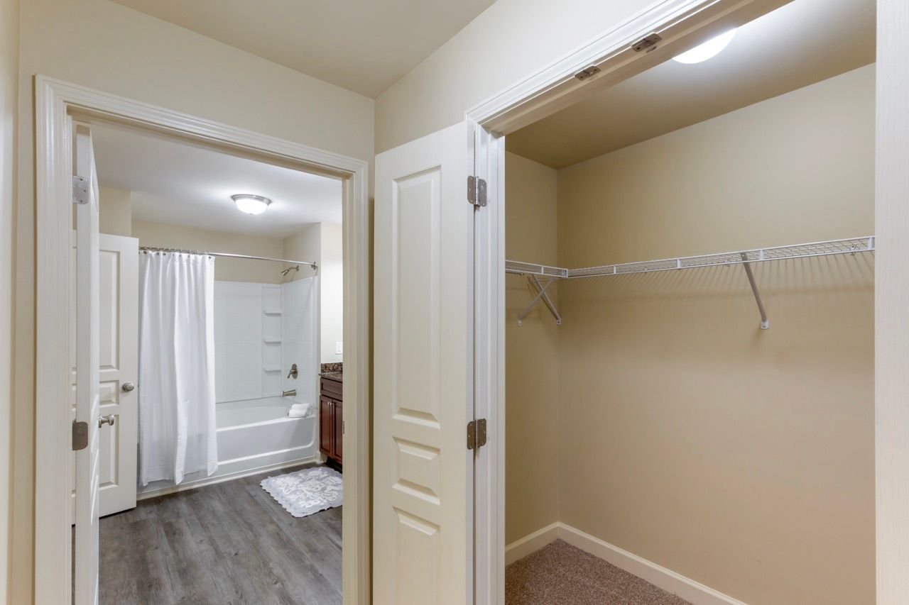 Bathroom with bathtub/shower, white curtain, and a nearby open closet with a wire shelf.