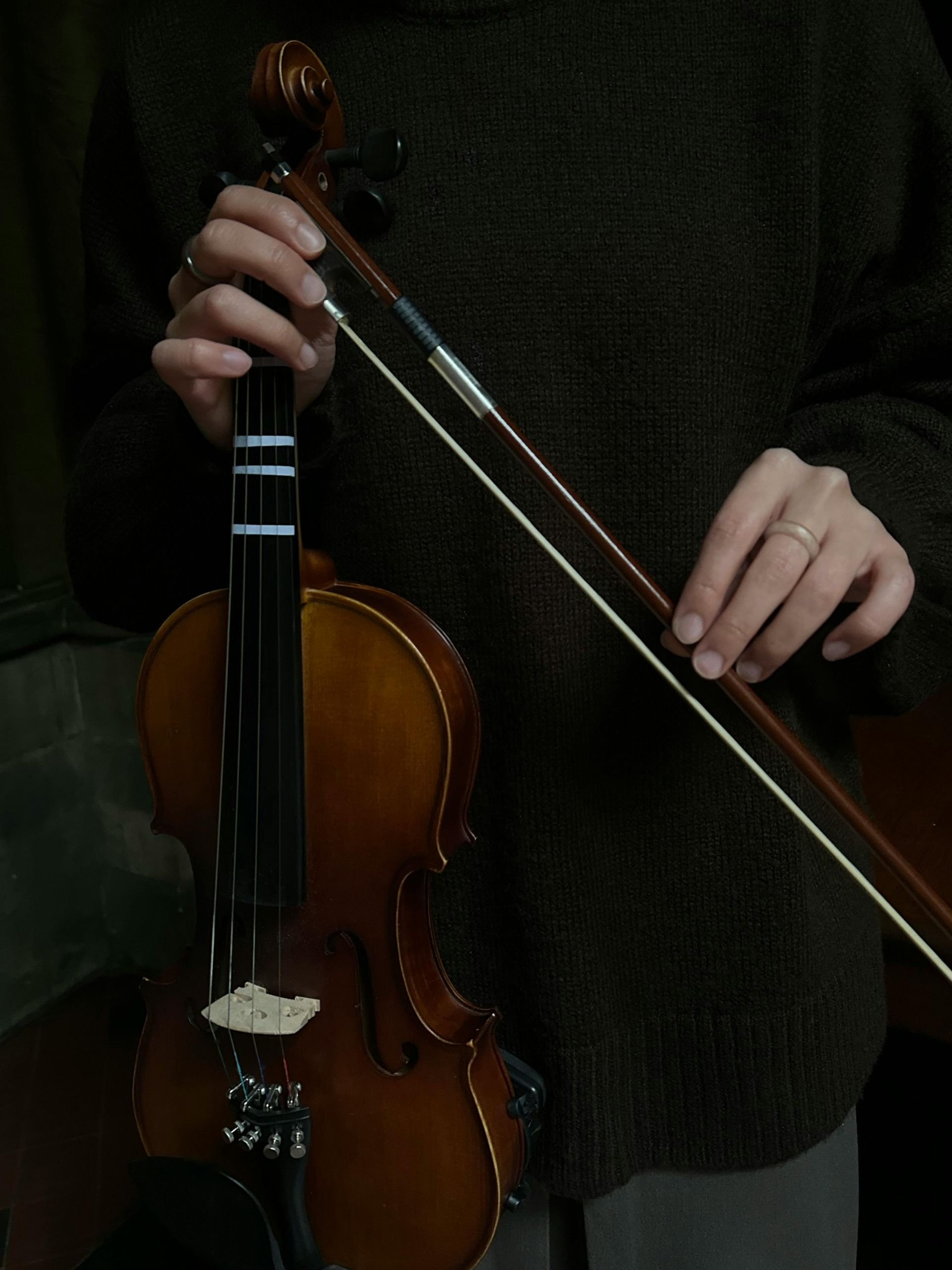 A person holding a violin in one hand and a bow in the other while wearing a dark-textured sweater.