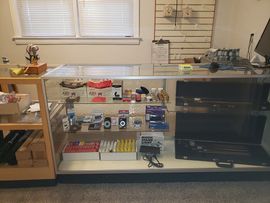A glass display case in a retail shop featuring shelves stocked with electronics, small goods, and boxes.