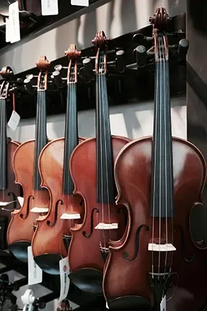 A row of brown wooden violins hanging on a display rack in a store.
