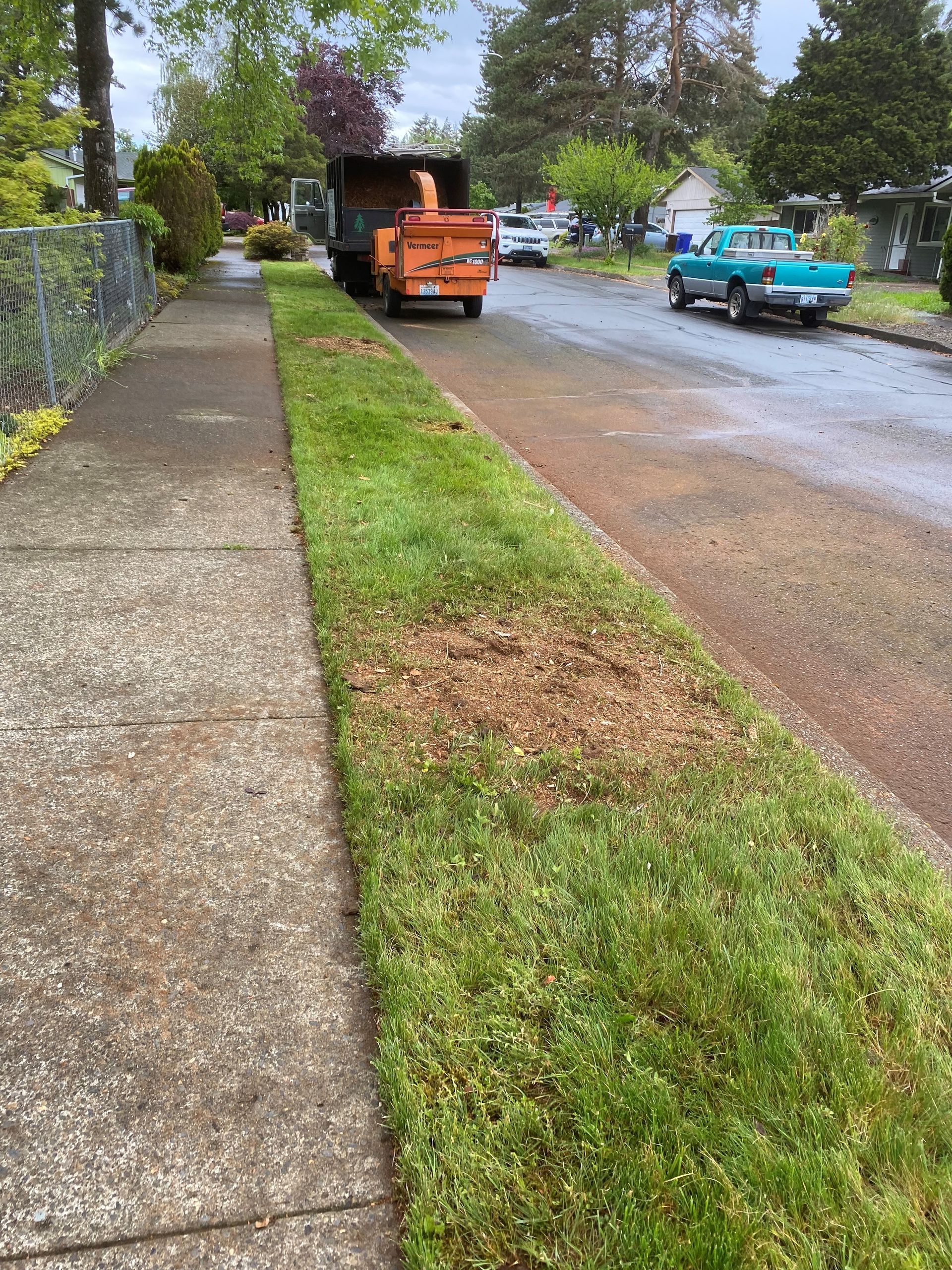 A tree chipper is sitting on the side of the road next to a sidewalk.