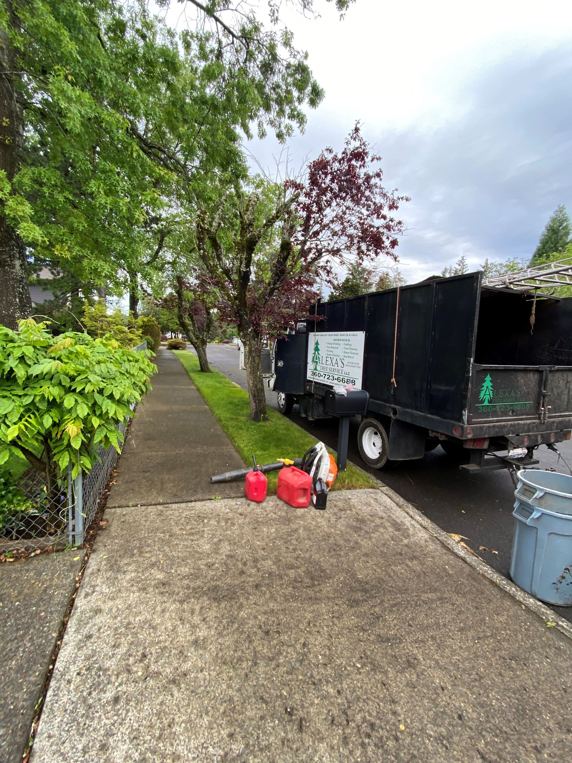 A dump truck is parked on the side of the road next to a sidewalk.