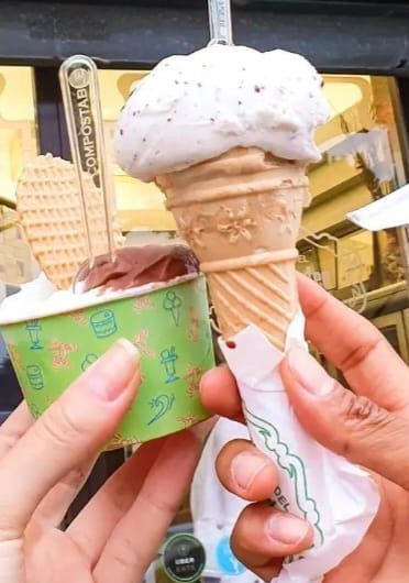 Una persona tiene in mano un cono gelato e una coppa di gelato