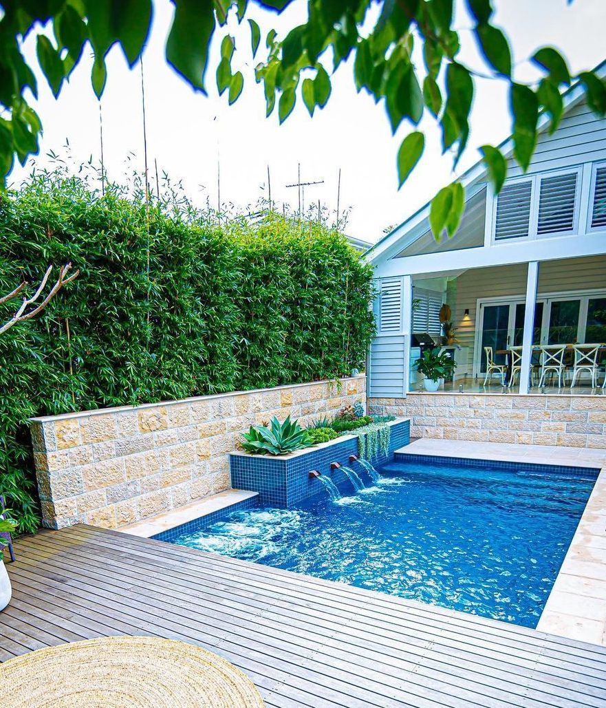 A Waterfall On A Stone Wall going Into A Pool With 2 Chairs On A Patio — Amber North Coast In Port Macquarie, NSW