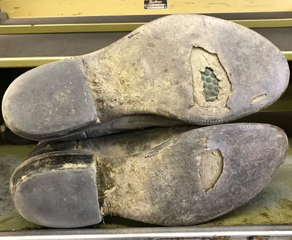 A pair of shoes with holes in the soles are sitting on a table.