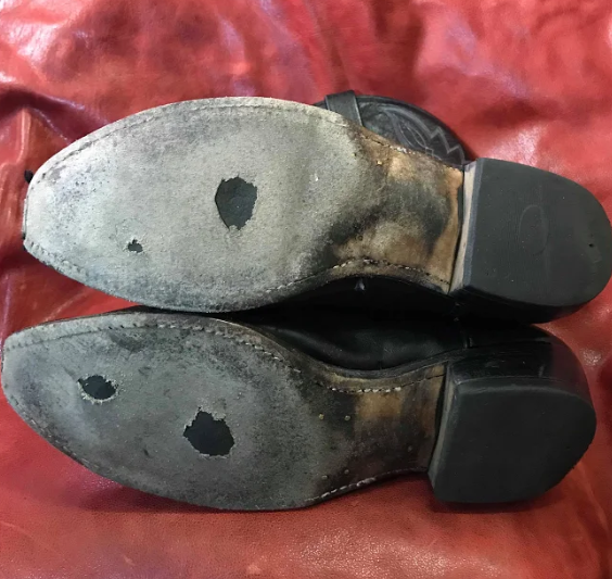 A pair of black cowboy boots with holes in the soles