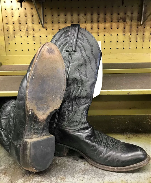 A pair of black cowboy boots are sitting on a shelf.