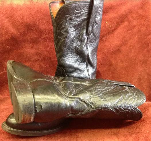 A pair of black cowboy boots are sitting on top of each other on a brown surface.