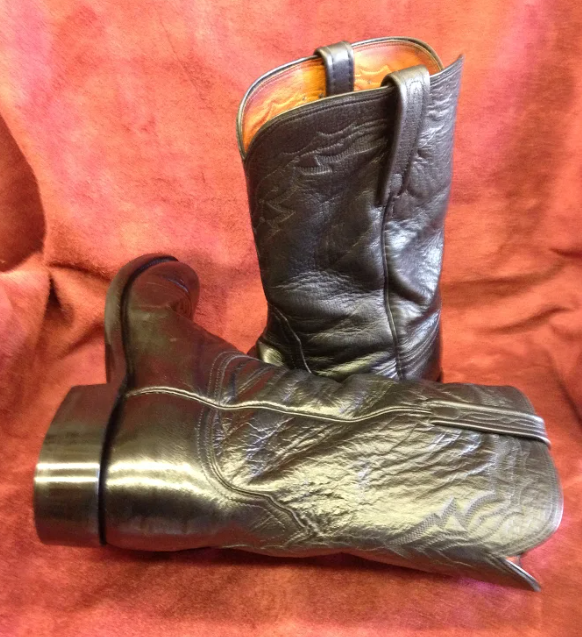 A pair of black cowboy boots are sitting on a red cloth.