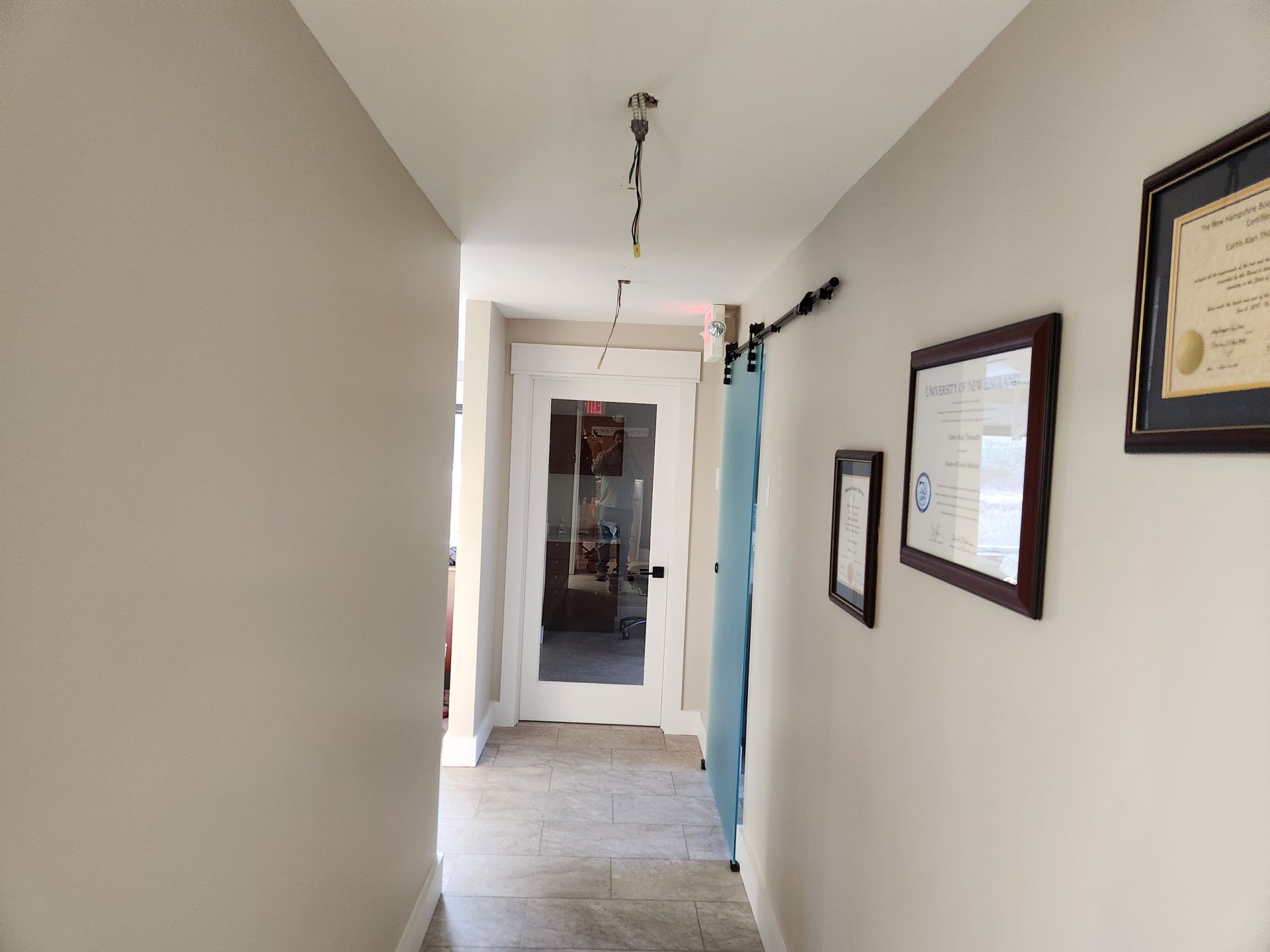 A long hallway with a glass door and framed pictures on the wall.
