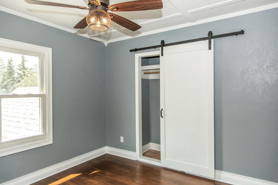An empty bedroom with a sliding barn door and a ceiling fan.