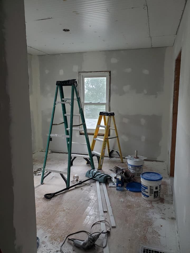 A room with a ladder and buckets of paint on the floor.