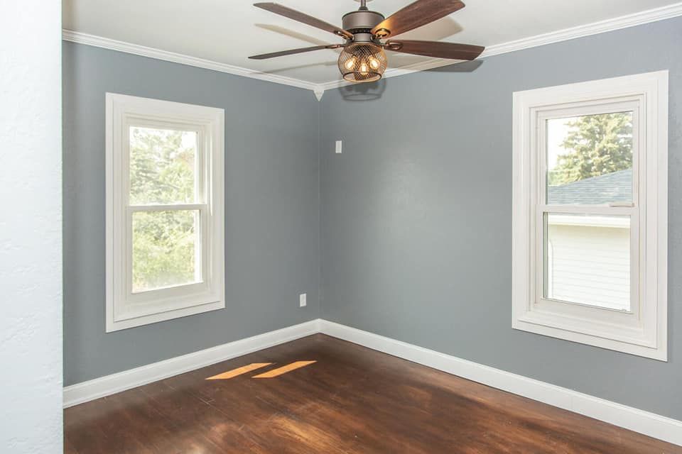 An empty room with a ceiling fan and two windows.