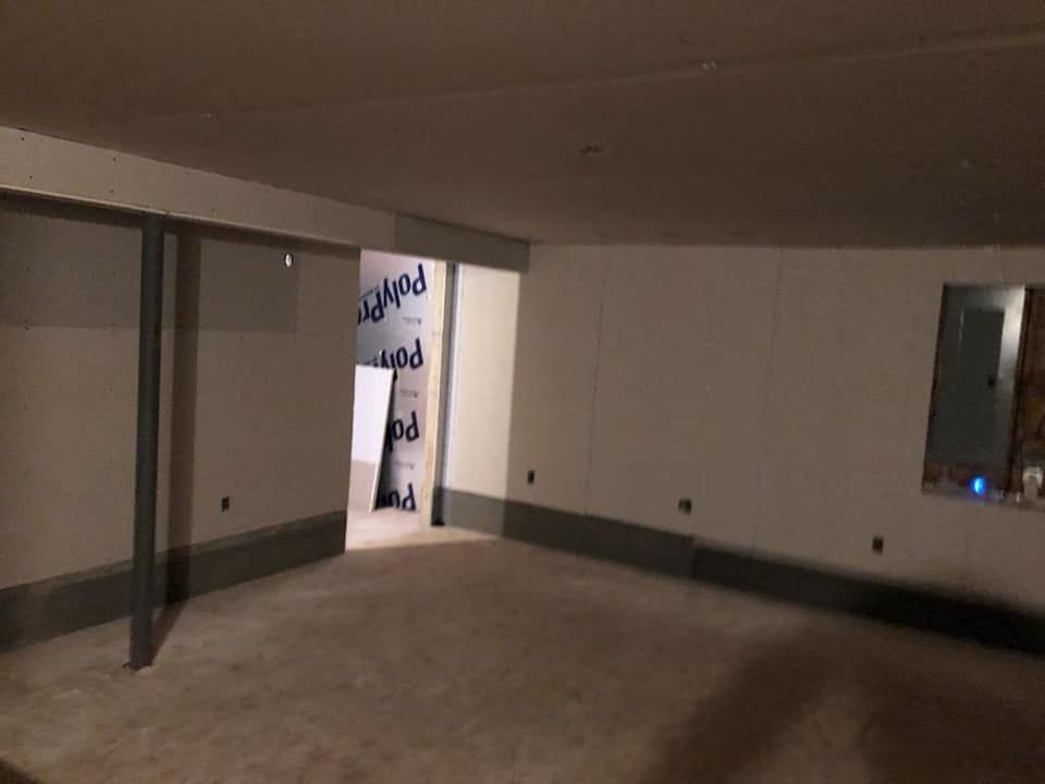 An empty basement with a carpeted floor and white walls.
