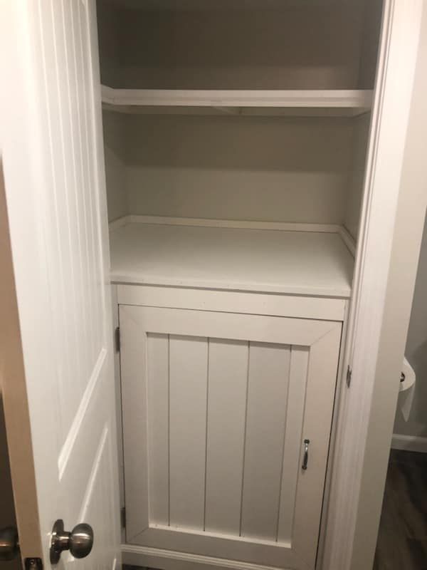 A white cabinet with shelves in a bathroom next to a toilet.