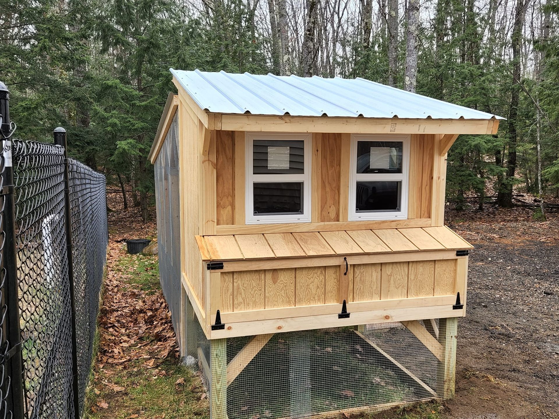 A wooden chicken coop with a metal roof is sitting next to a chain link fence.