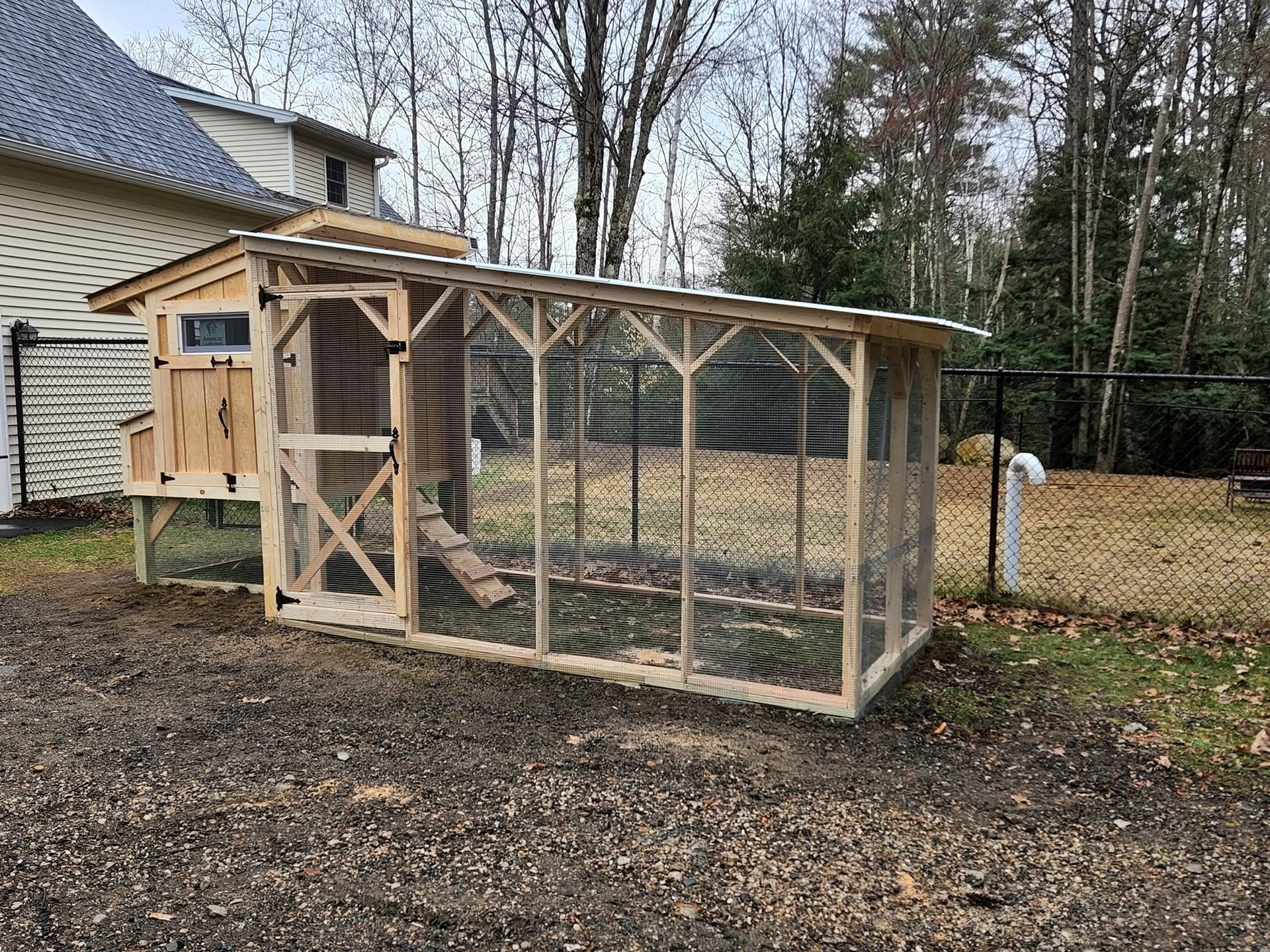 A wooden chicken coop is sitting in the dirt in front of a house.