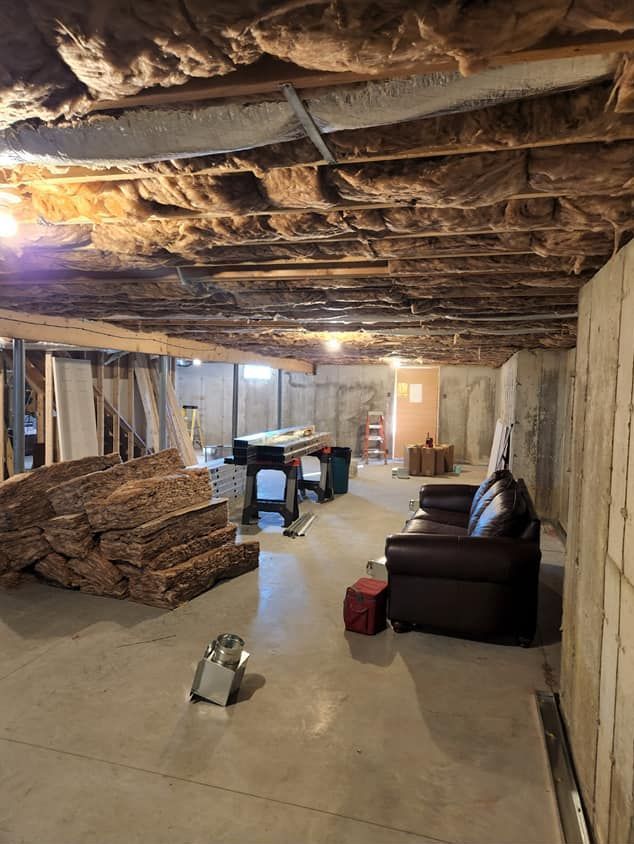 A basement with insulation on the ceiling and a couch and chair.