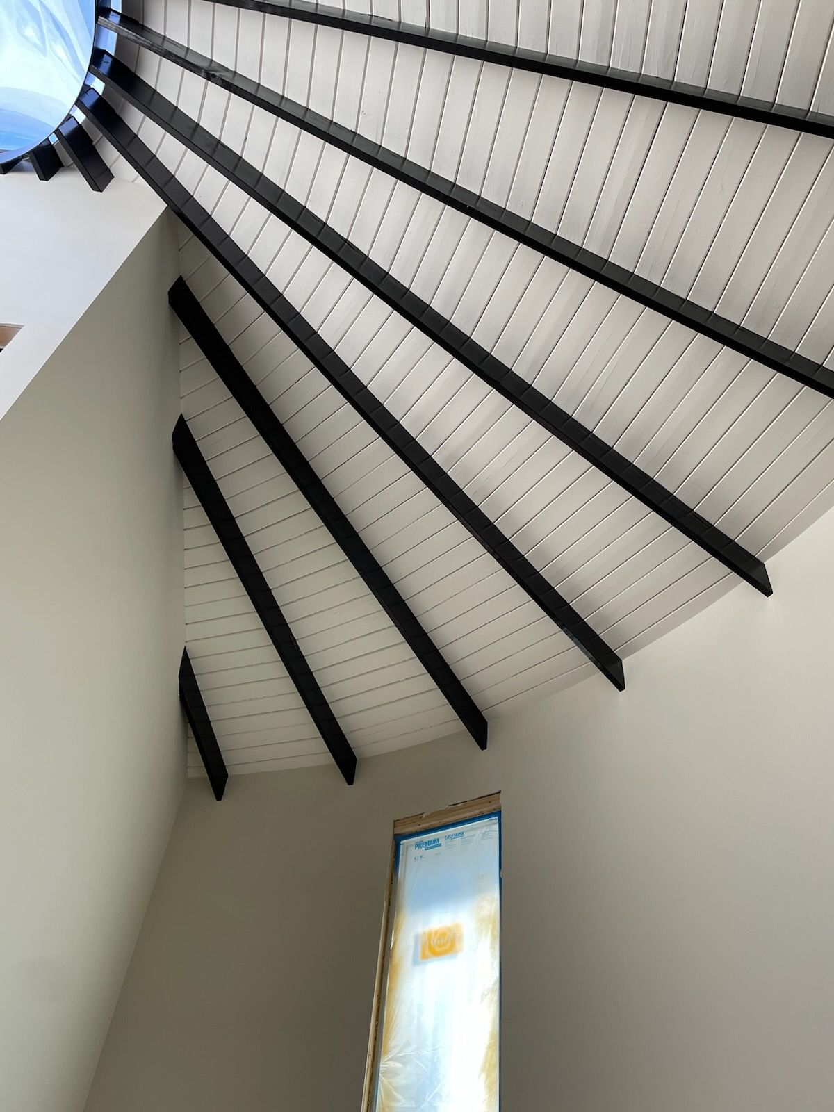 Looking up at a ceiling with black beams and a window.