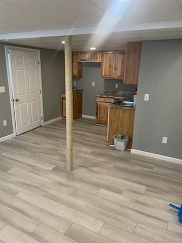 A basement with a kitchen and wooden cabinets.