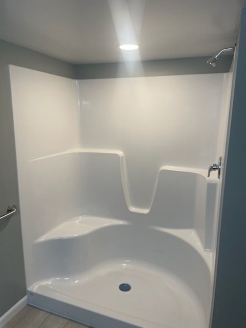 A white shower stall with a seat and a shower head in a bathroom.