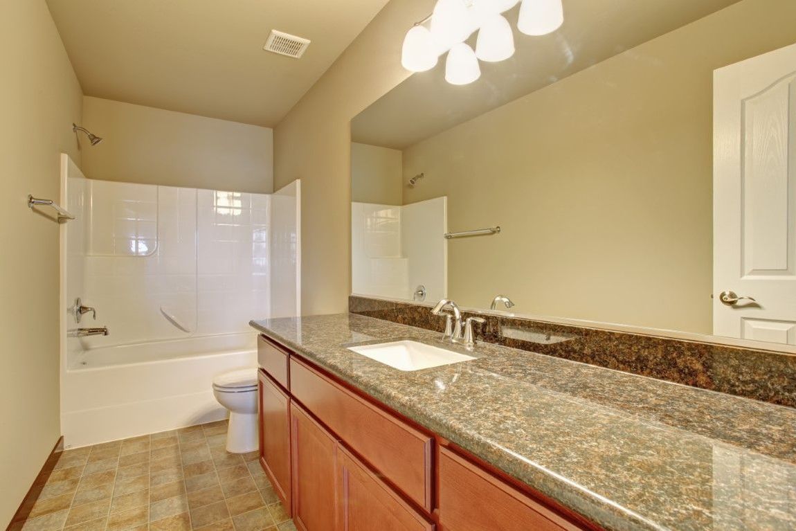 Bathroom with a bathtub, toilet, sink, and brown cabinets; beige walls and tile floor.