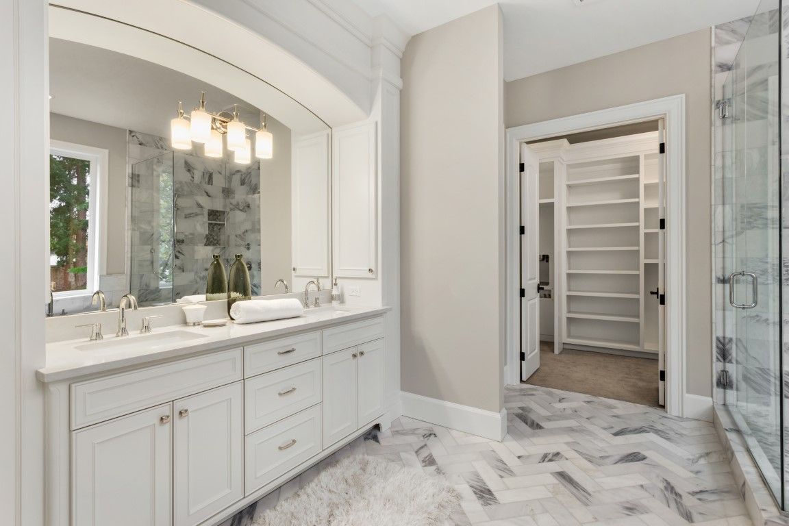 White bathroom with vanity, walk-in closet, and glass shower. Herringbone tile floor.