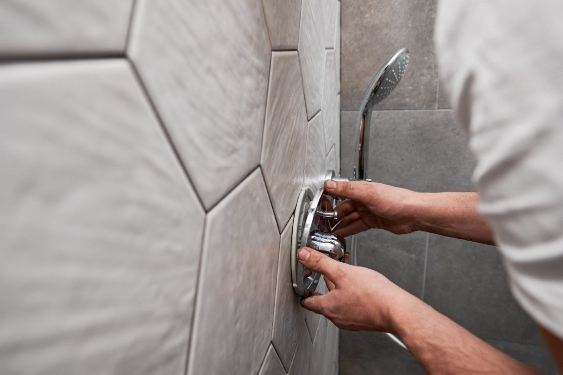 Person installs a shower faucet on tiled wall; focus on hands and fixture.