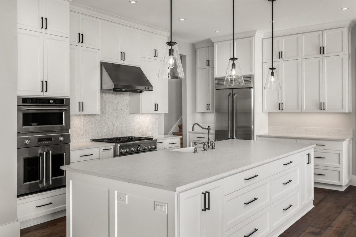 White modern kitchen with island, stainless appliances, dark hardware, and pendant lights.