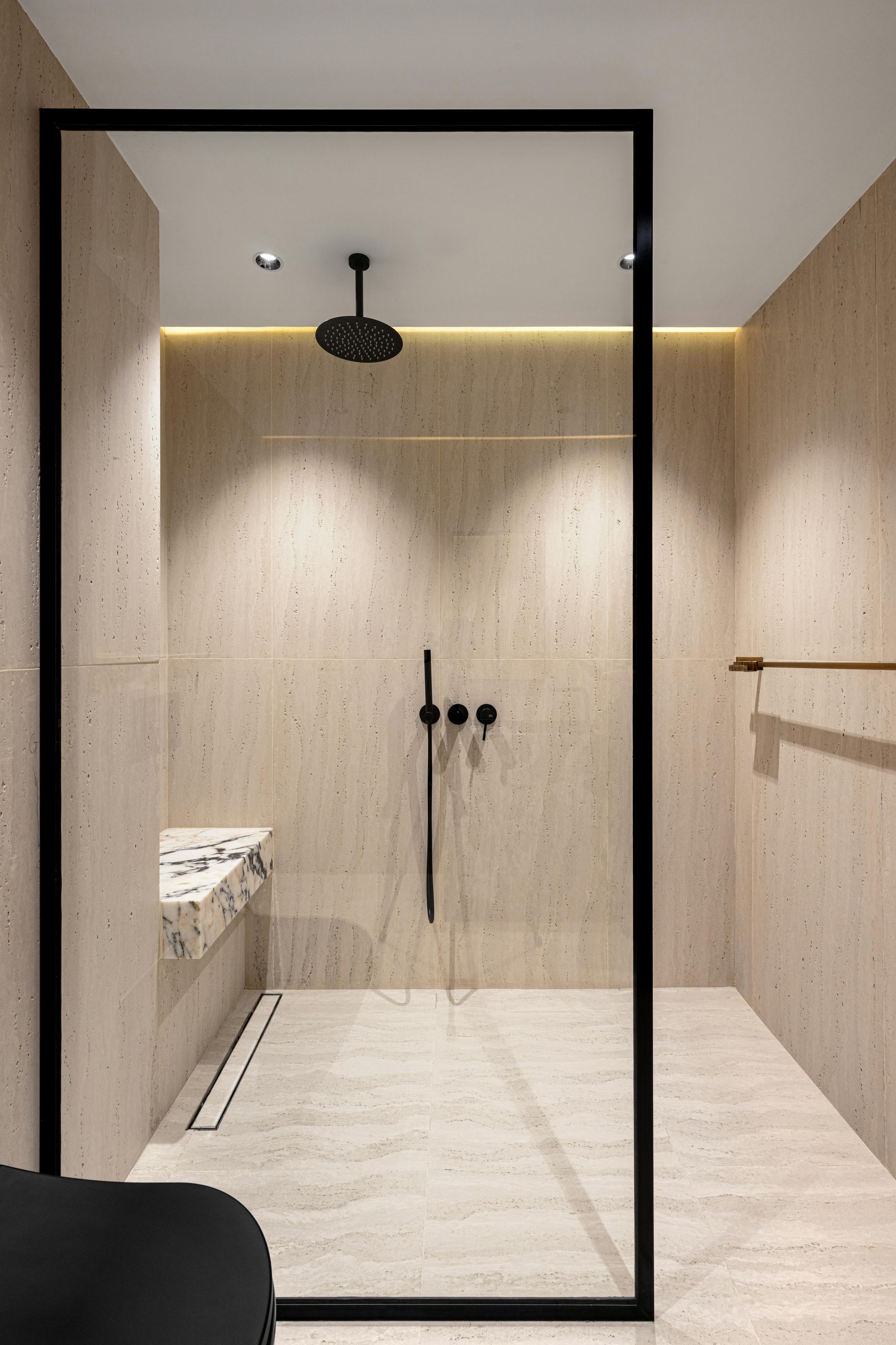 Walk-in master shower with large wall panels, built-in bench seating, and modern black fixtures designed for daily comfort.