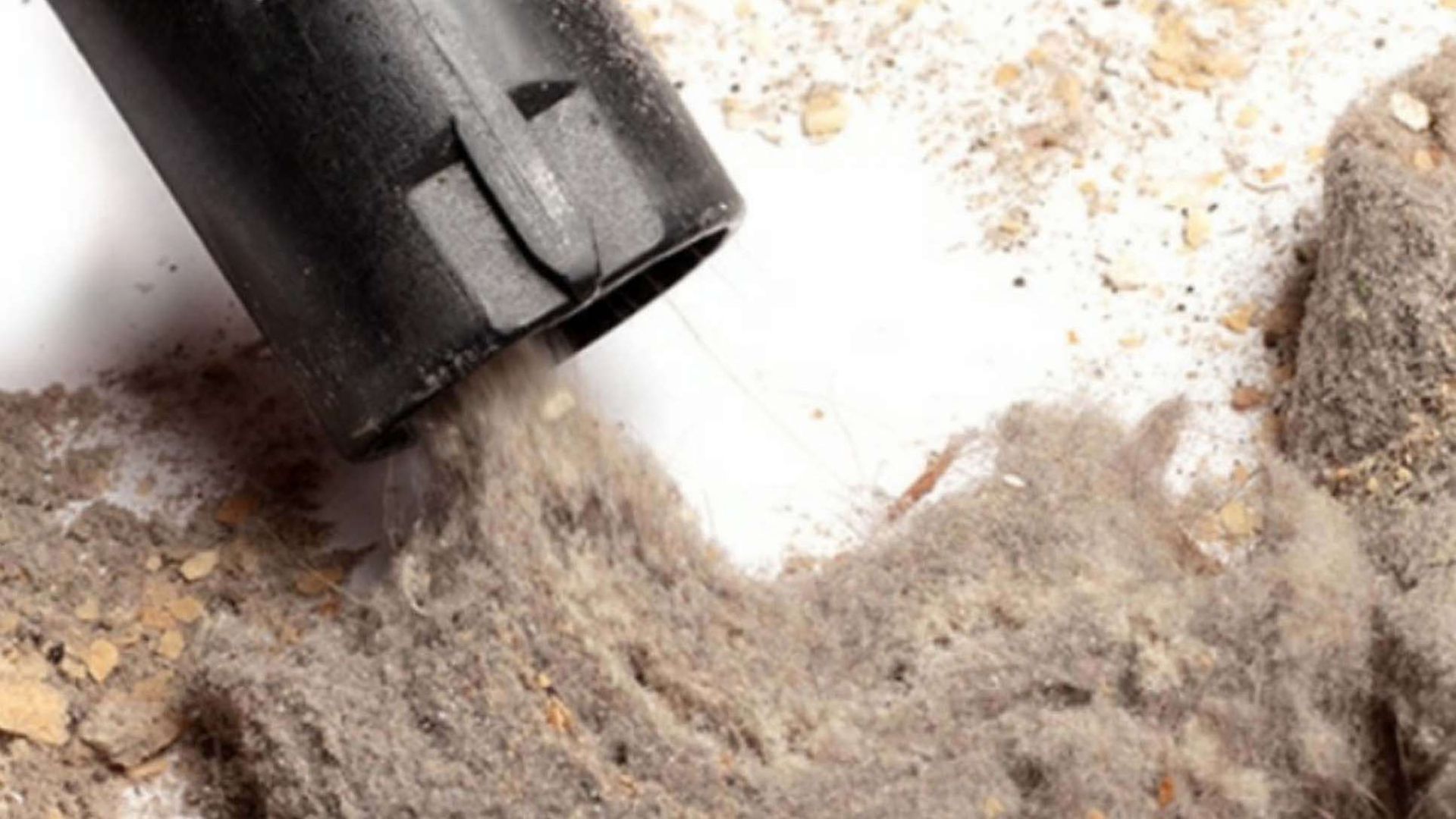 A vacuum cleaner is cleaning a pile of dust on a white surface.