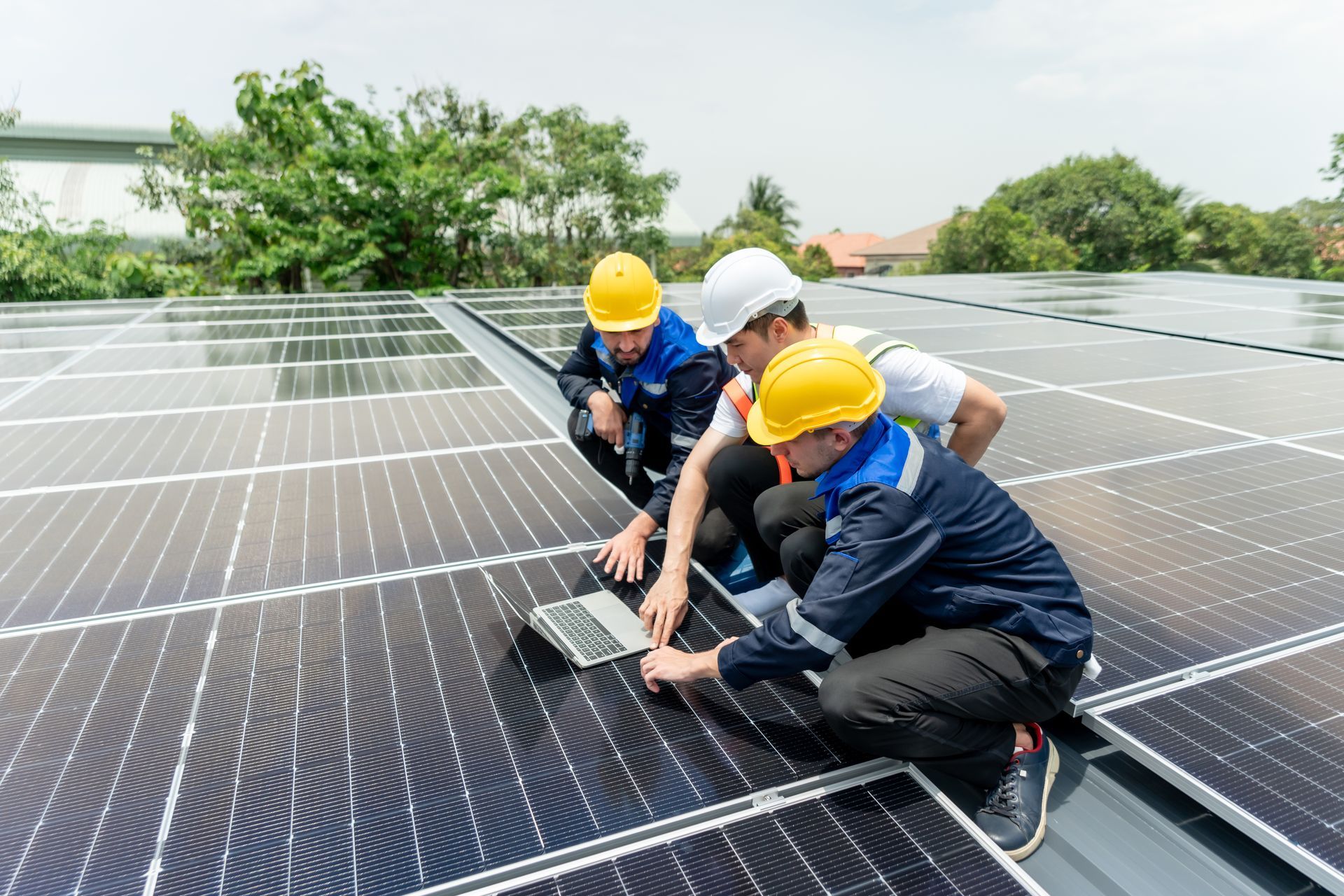 Three solar panel technicians inspecting a solar panel array on a rooftop, using a laptop