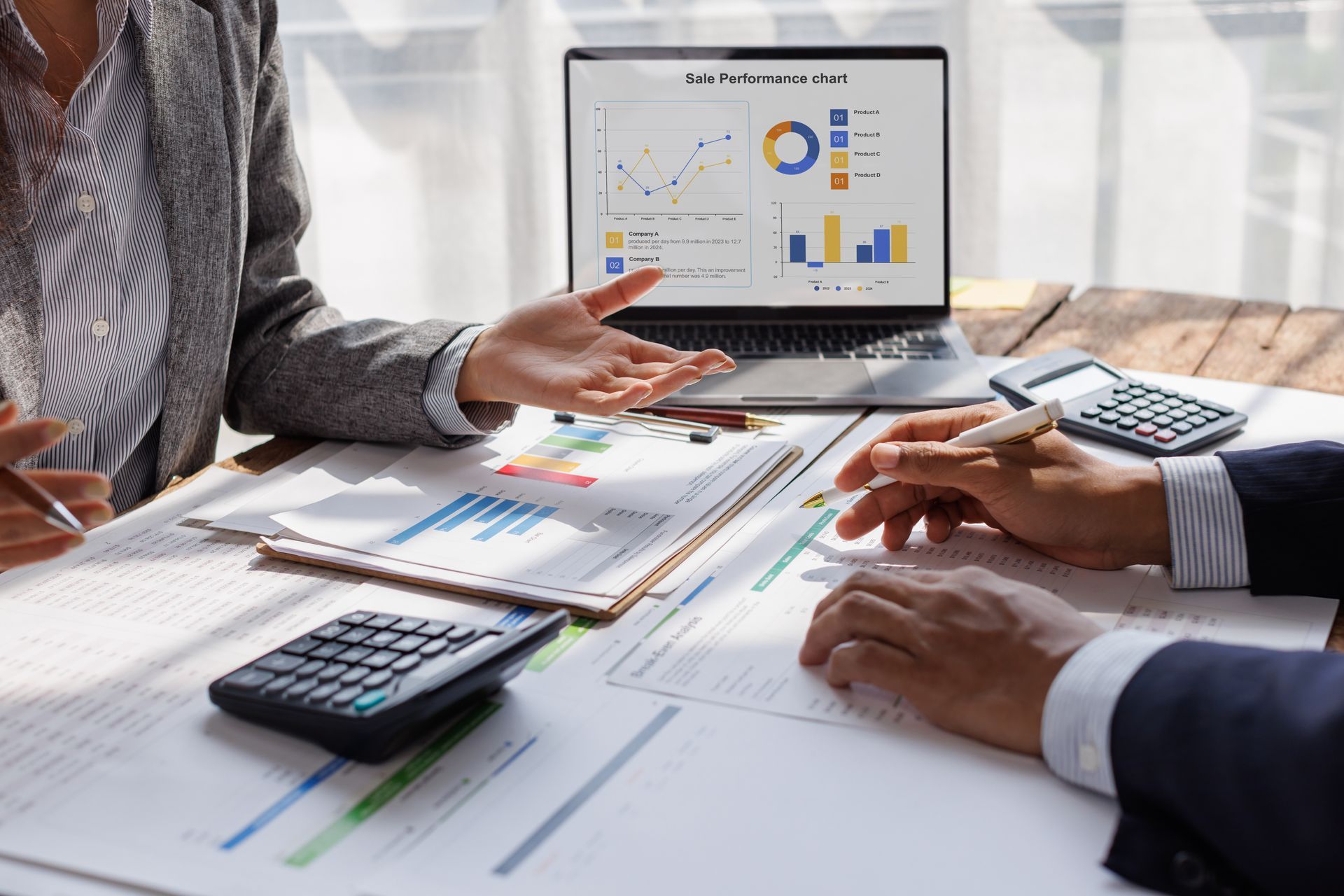 Two people reviewing financial reports with a laptop displaying charts and graphs, and two calculators