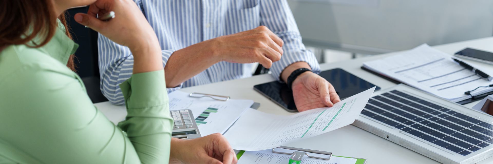 Two people reviewing financial documents at a desk, light clothing Two people reviewing financial documents at a desk, light clothing