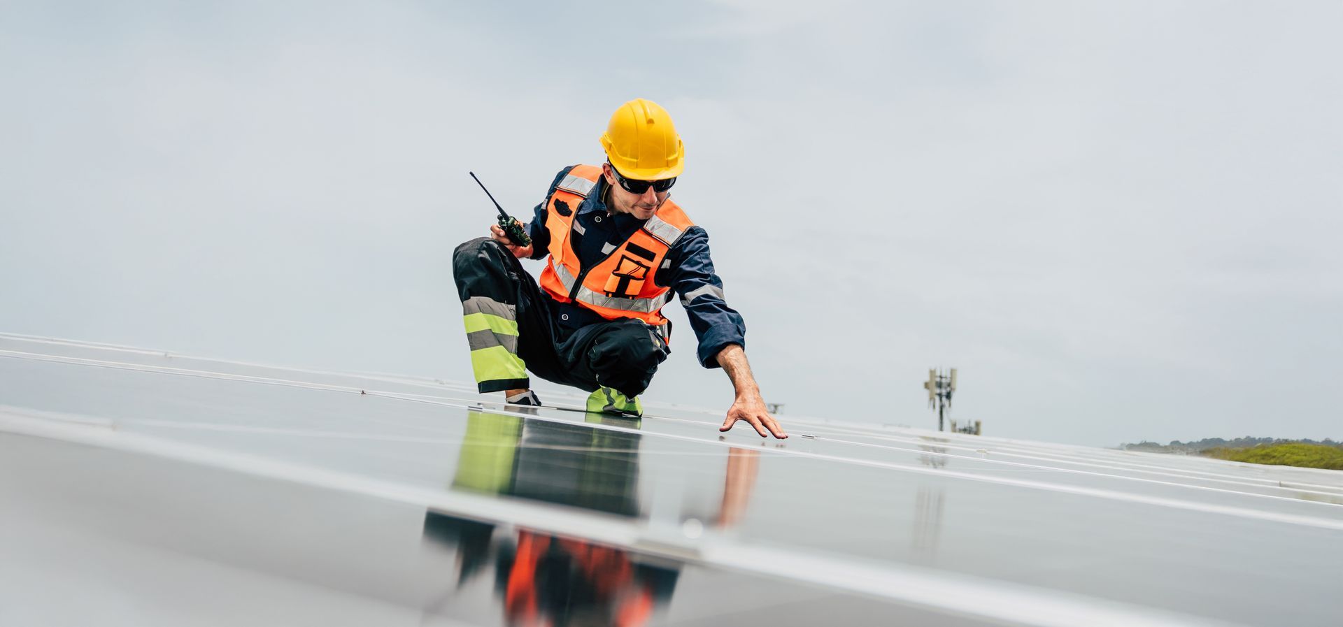 A worker in safety gear inspects solar panels on a rooftop