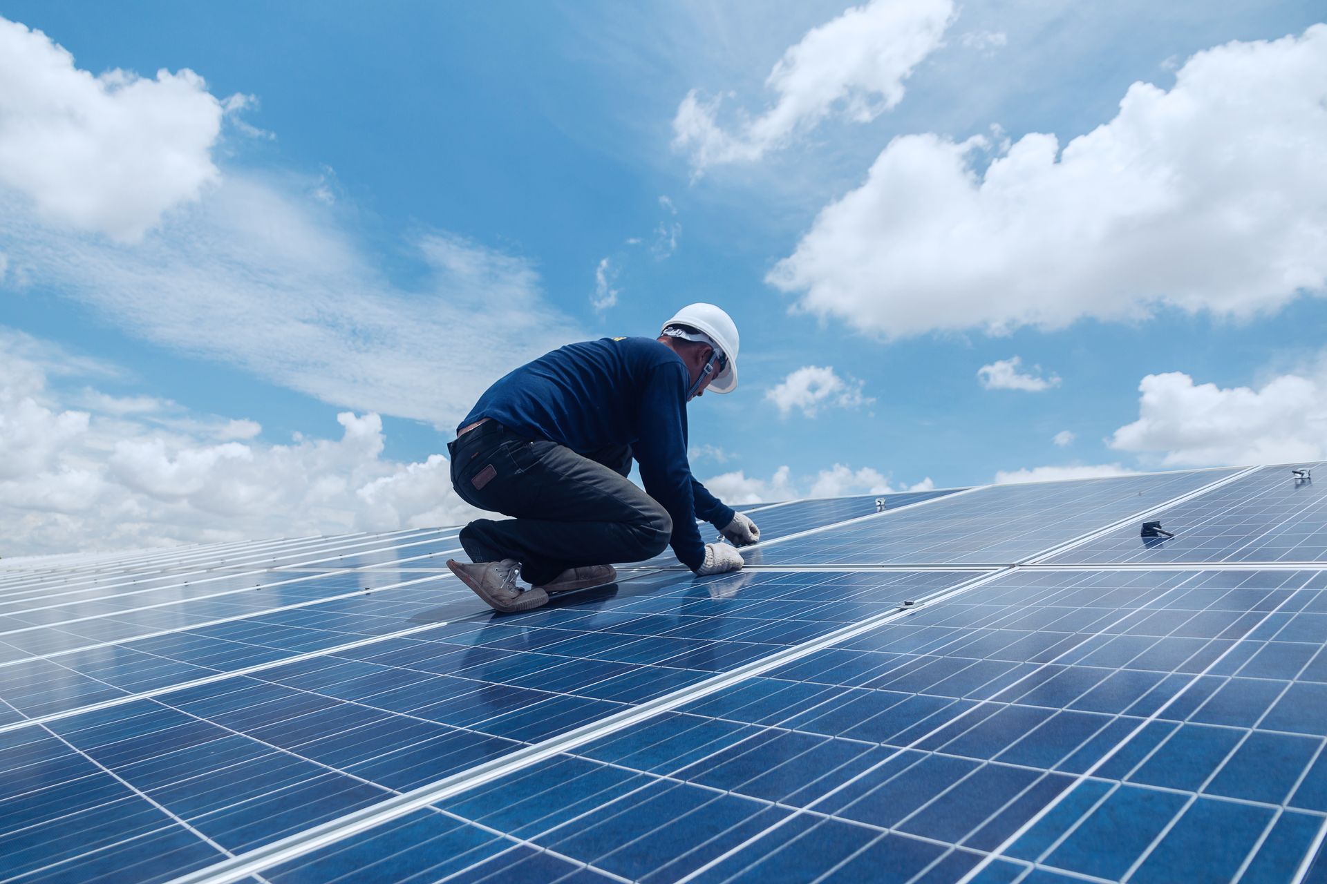 A worker in safety gear inspects solar panels on a rooftop