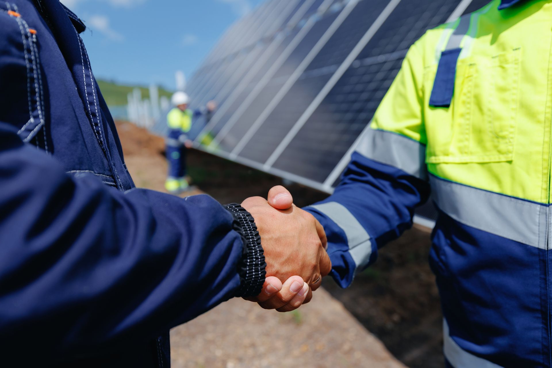 Two construction workers shaking hands in front of a solar panel array Two construction workers shaking hands in front of a solar panel array