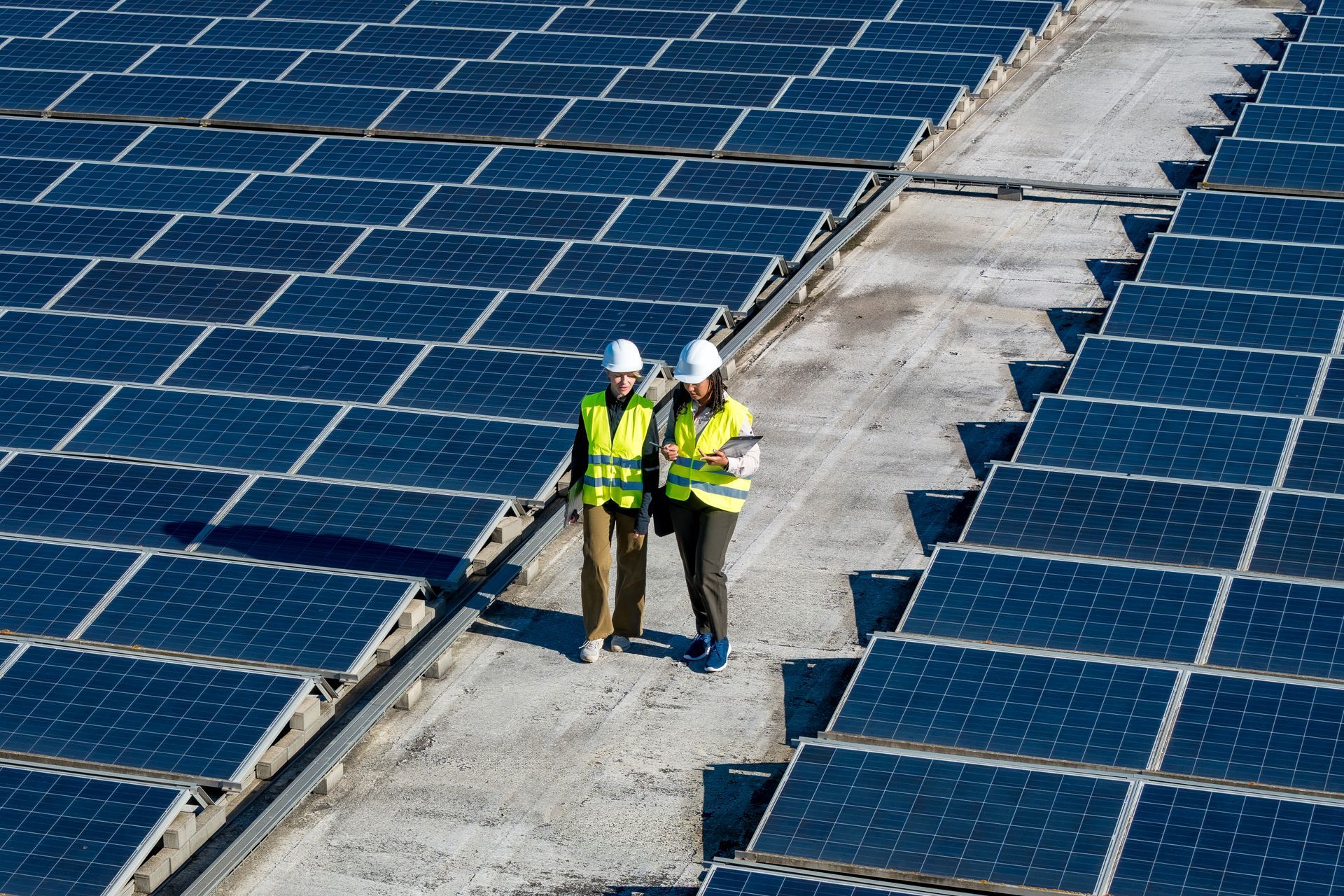 Two people in safety vests and hard hats on a rooftop solar panel array