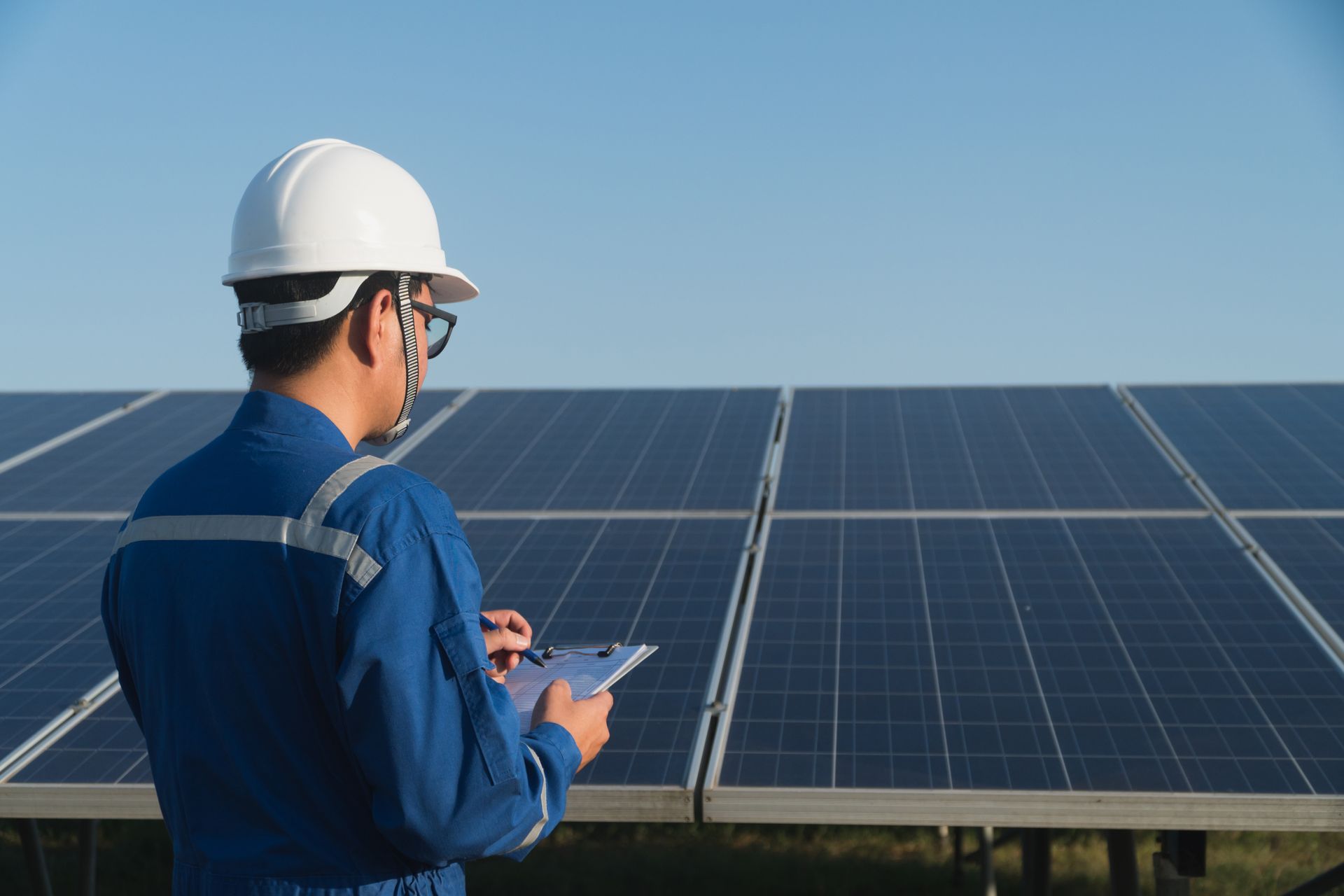 Person in blue work suit and hard hat examines solar panels under a blue sky