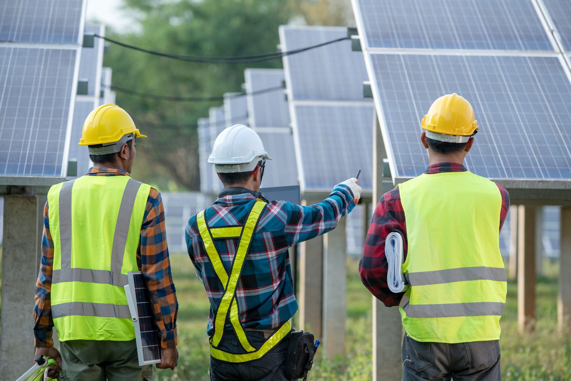 Three workers in safety vests and helmets inspect solar panels