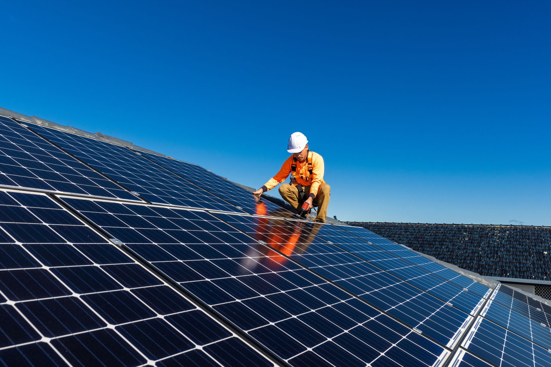Solar panel installer working on rooftop under a clear blue sky