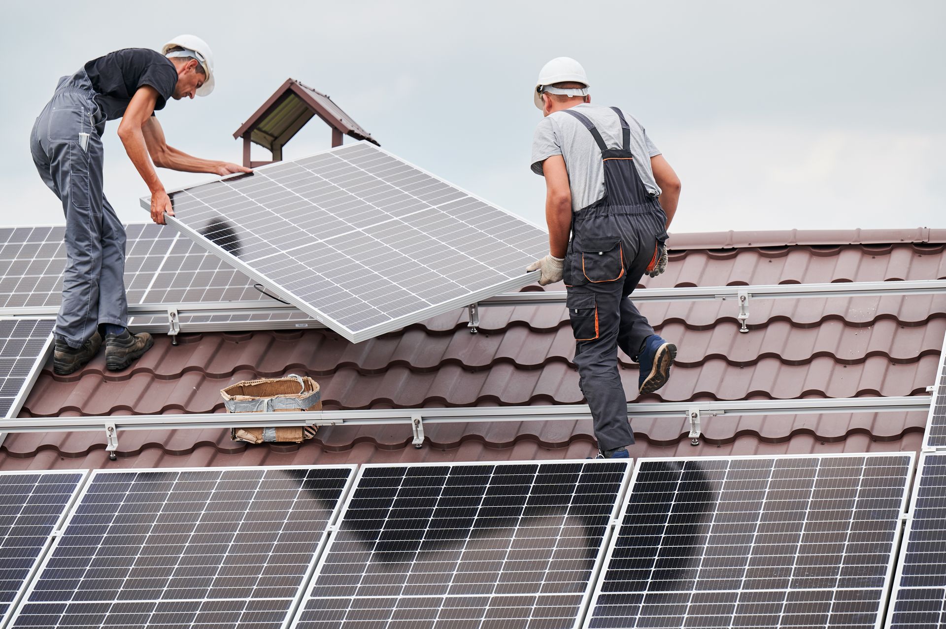 Two workers installing a solar panel on a rooftop