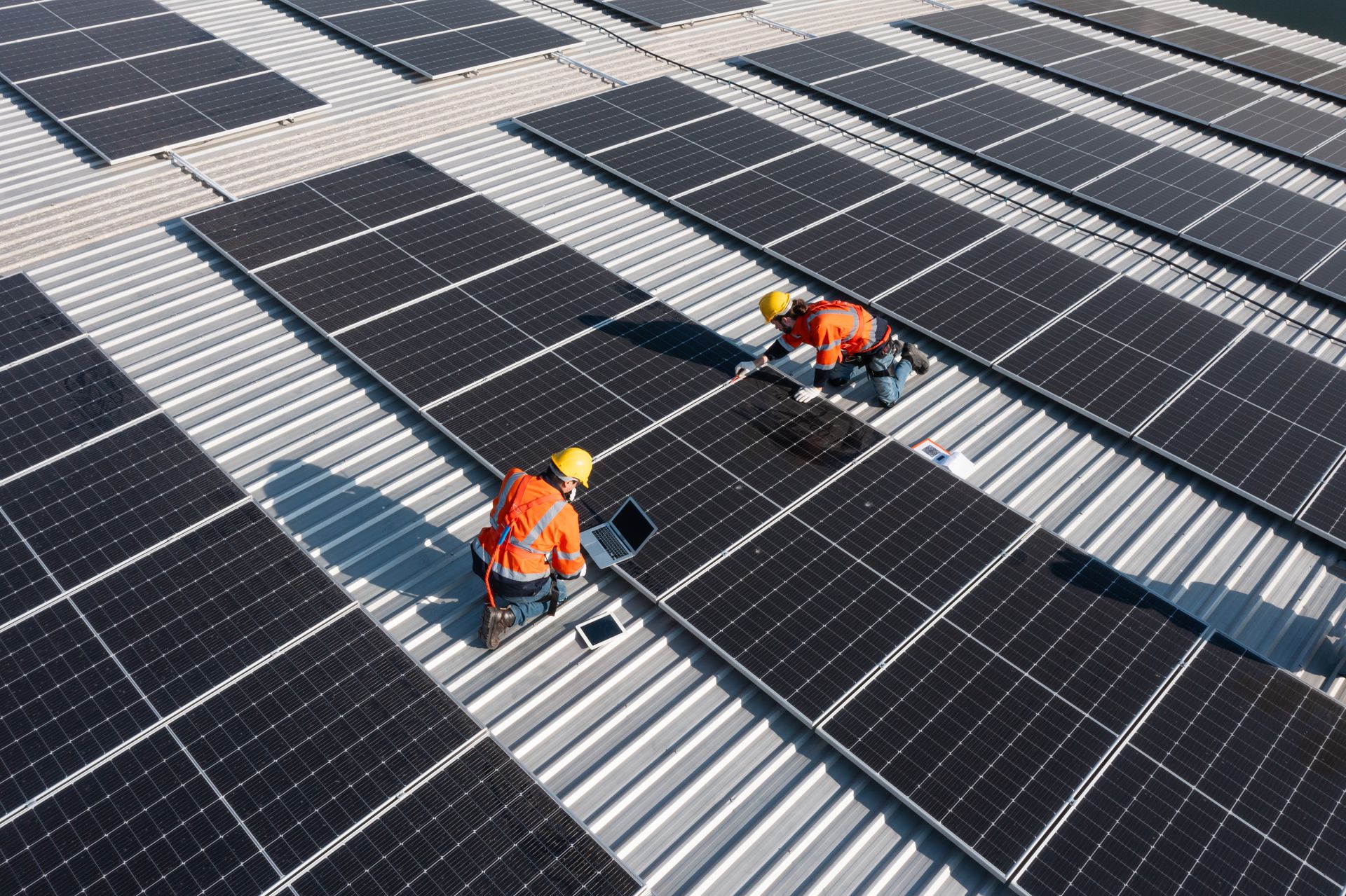 Workers in orange vests installing solar panels on a metal roof