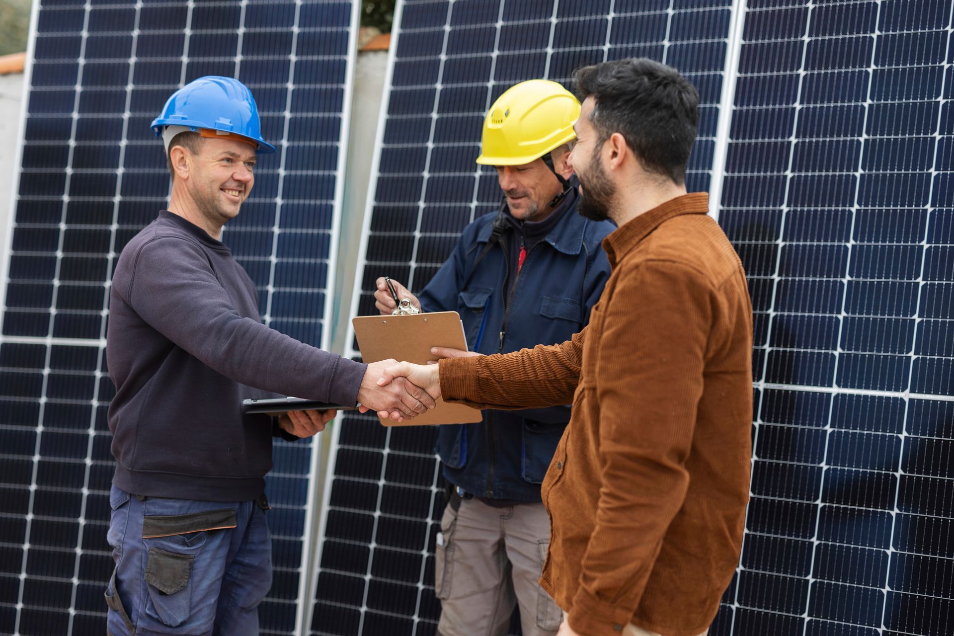 Three men shaking hands next to solar panels Three men shaking hands next to solar panels